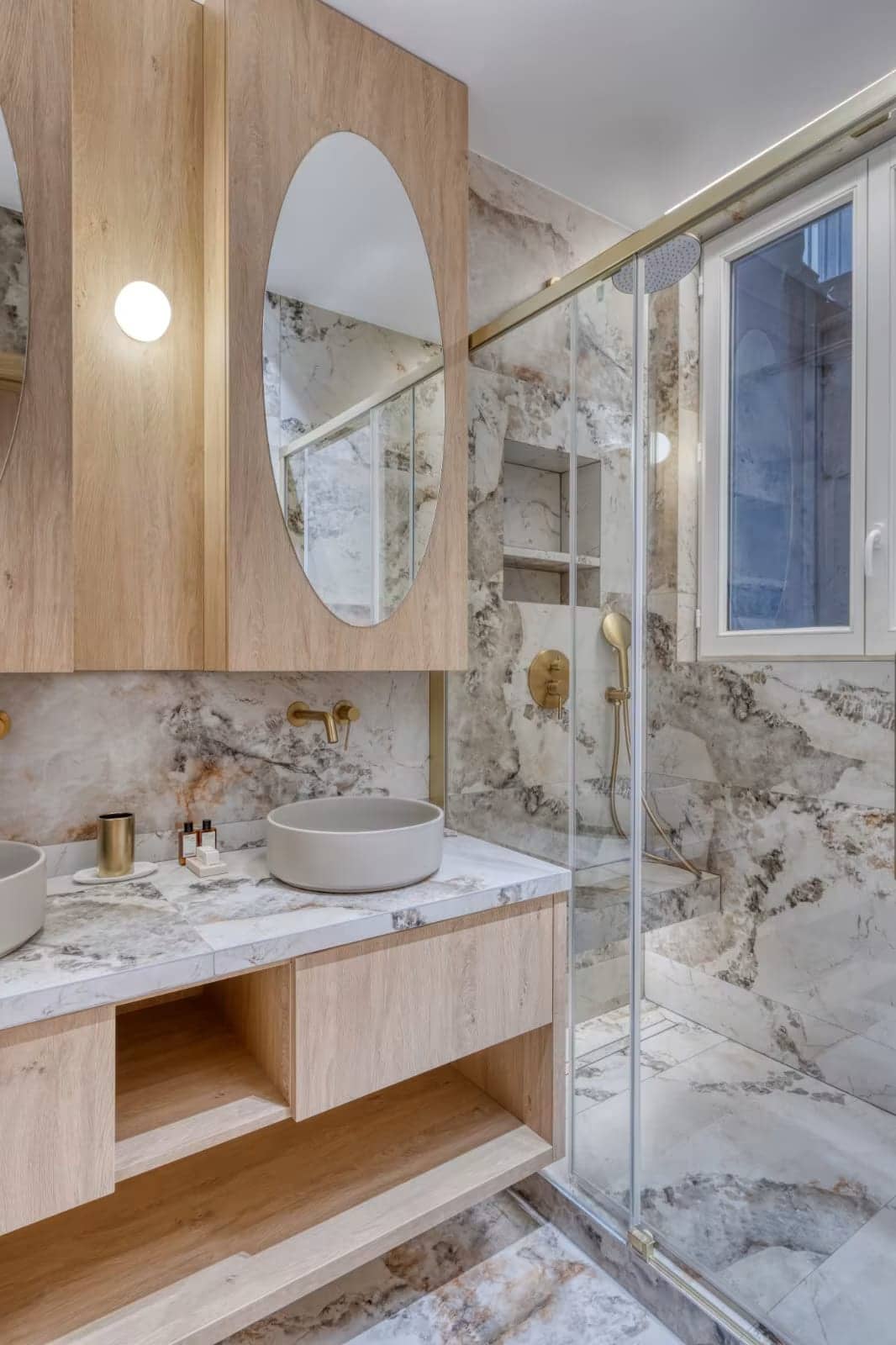 Salle de bain en pierre veinée avec double vasque, meuble en chêne, miroirs ovales et douche