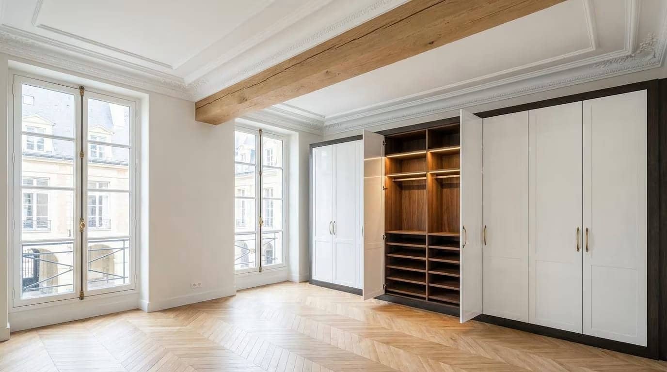 Chambre avec poutre en bois apparente, grand placard blanc ouvert et parquet en point de Hongrie