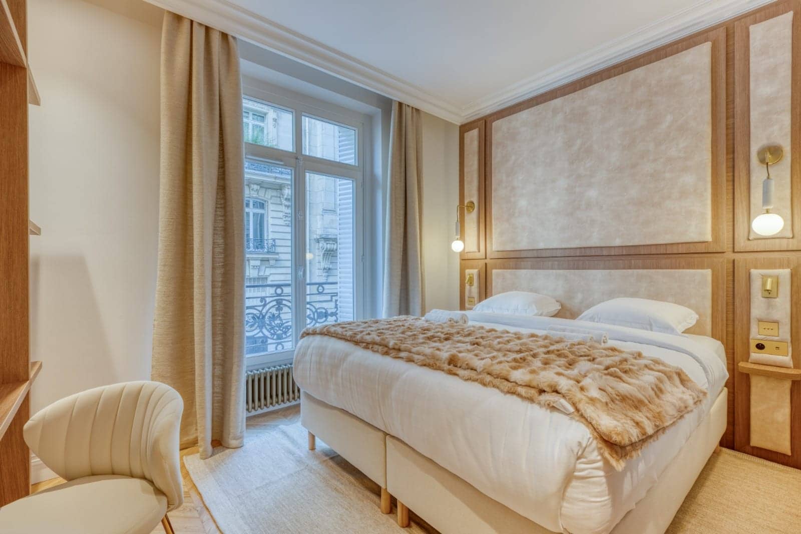 Chambre avec tête de lit capitonnée encadrée de chêne, plaid en fourrure et fenêtre sur balcon