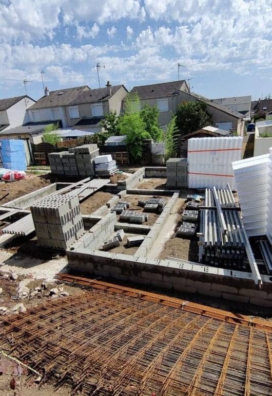 Chantier de fondations d'une maison avec parpaings, treillis soudé et palettes de matériaux