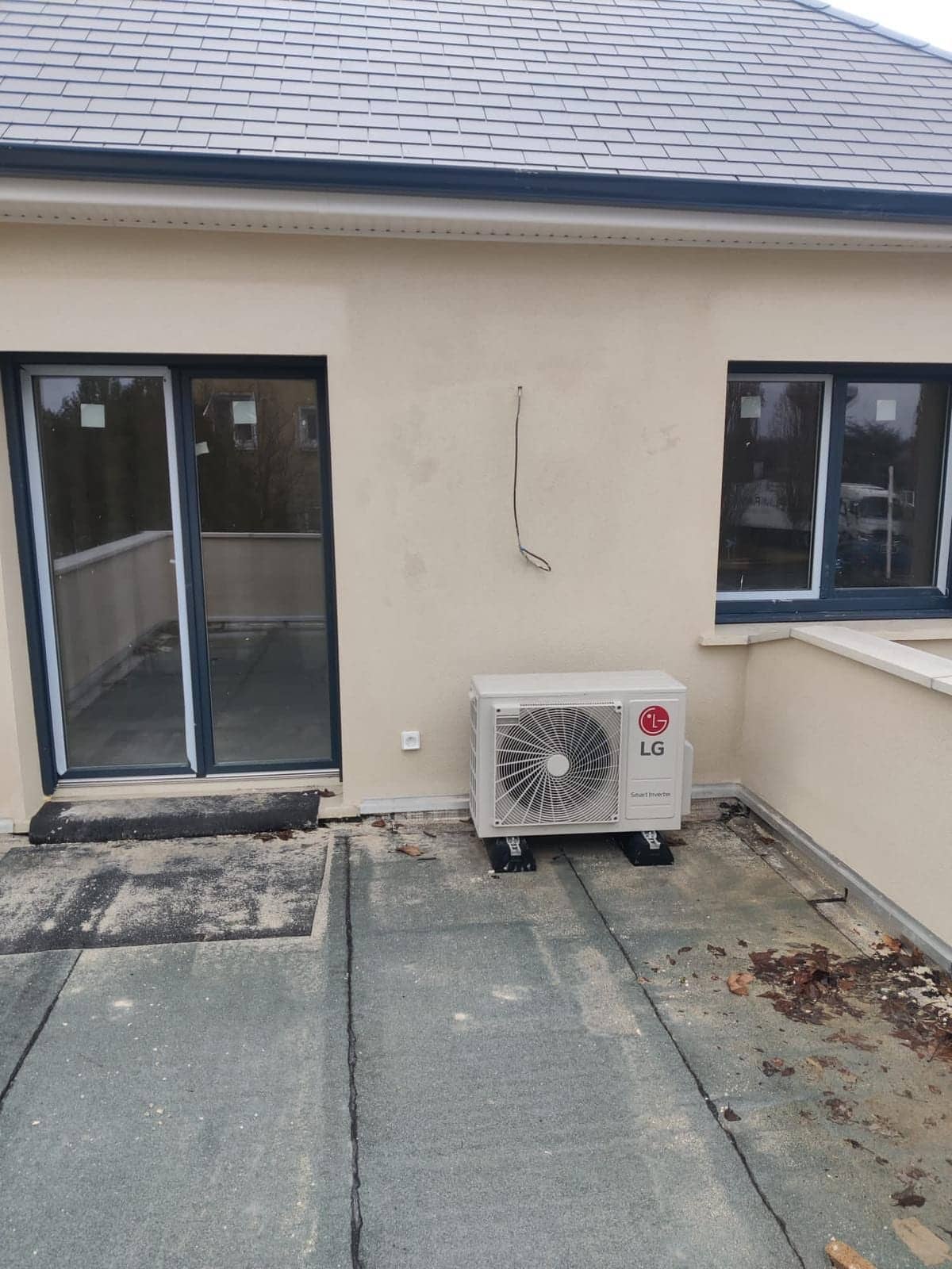 Groupe extérieur de pompe à chaleur LG fixé sur une terrasse devant une porte-fenêtre