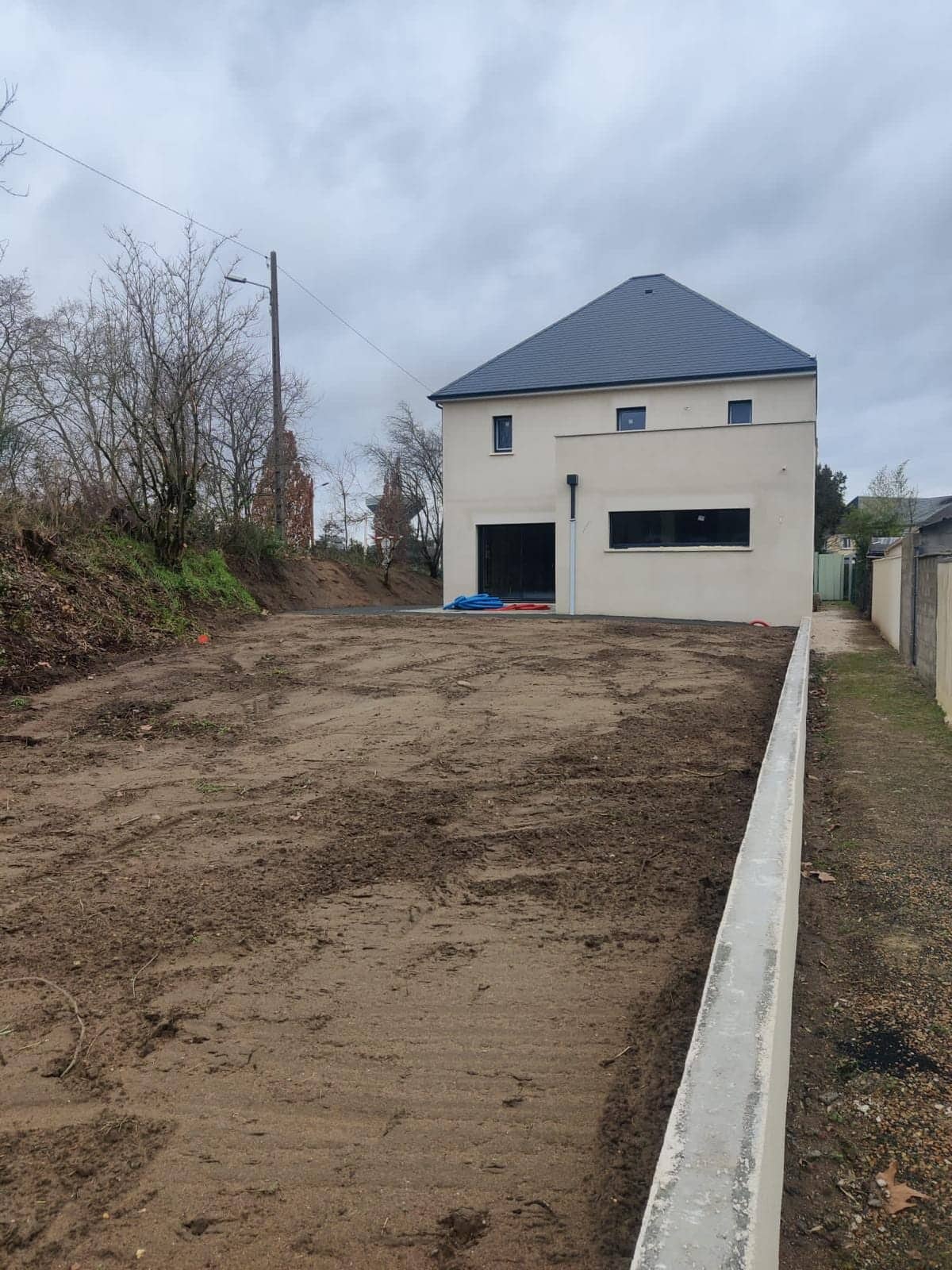 Pavillon neuf en cours de construction, façade enduite beige, toit en ardoise et terrain terrassé