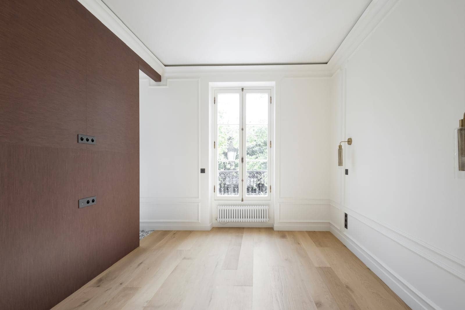 Chambre d'appartement à Versailles avec parquet clair, fenêtre sur balcon, boiseries blanches et mur brun