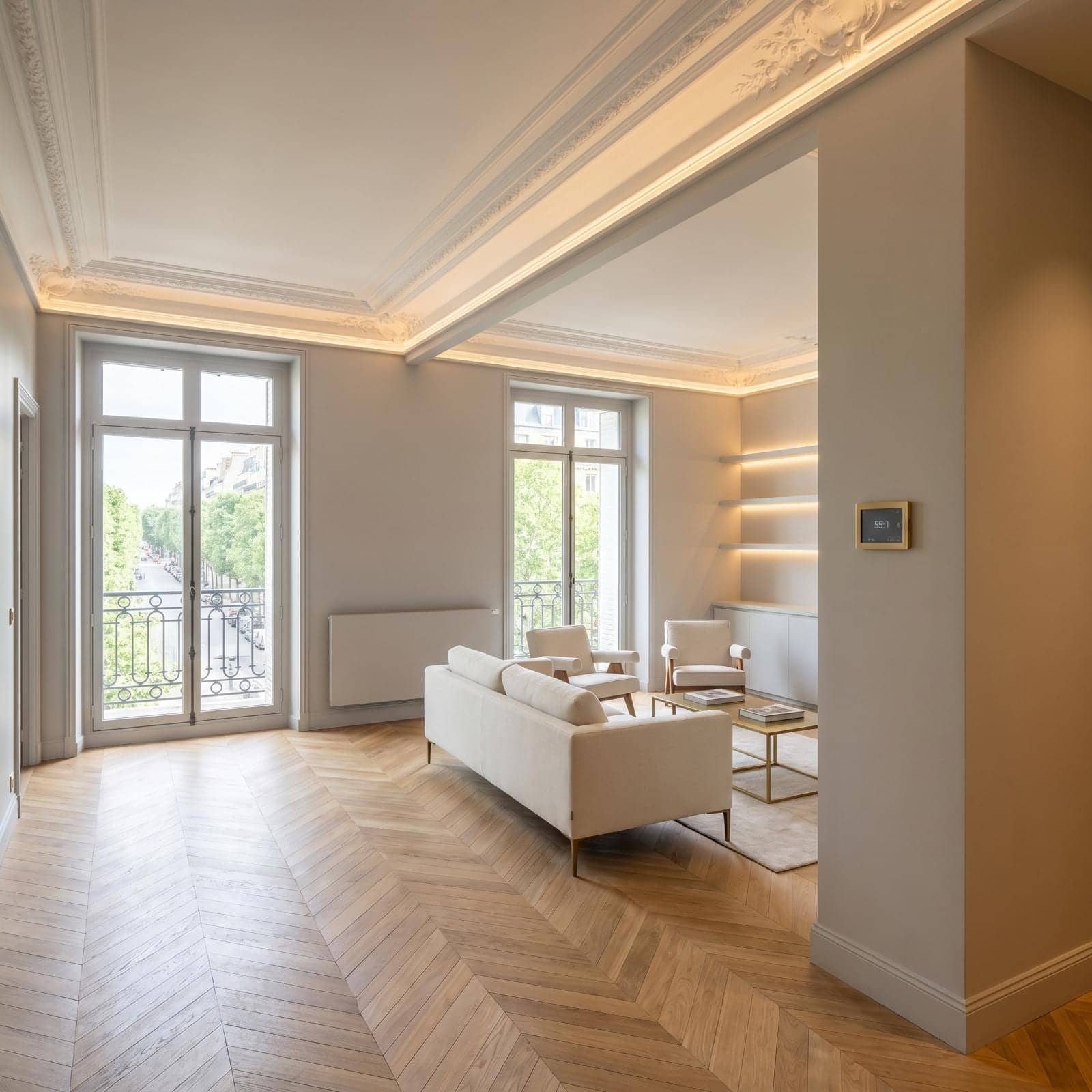 Salon haussmannien avec moulures, parquet en point de Hongrie, canapé blanc et corniche lumineuse à Neuilly-sur-Seine