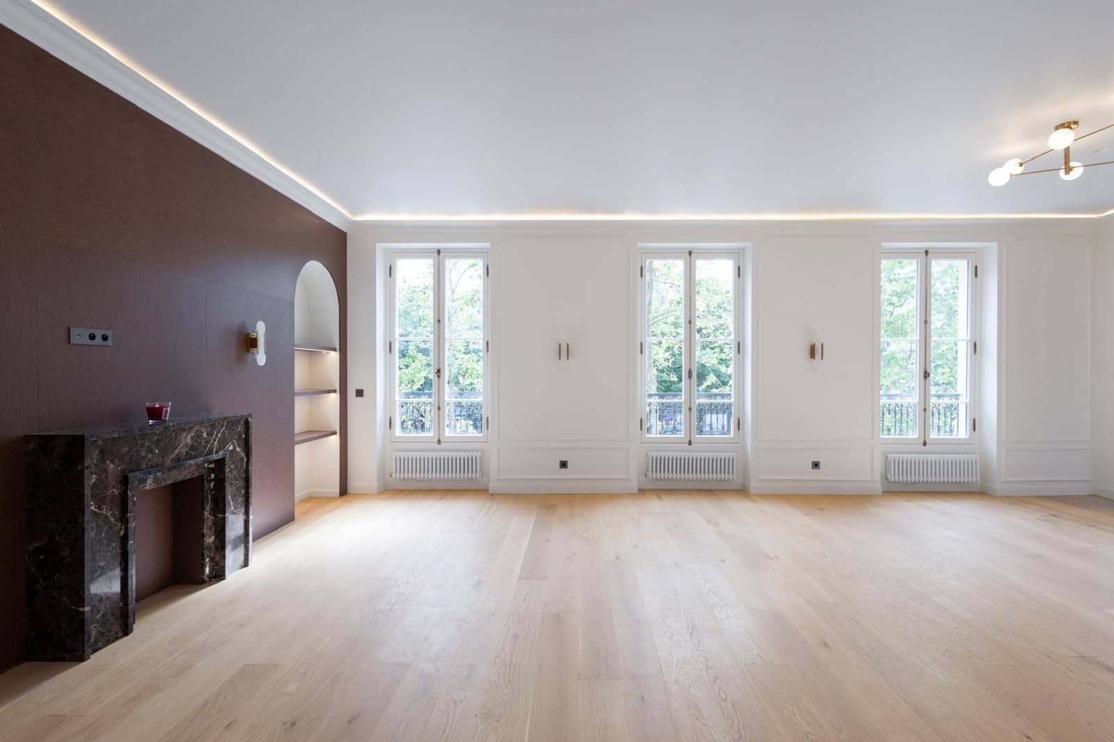 Salon à Versailles avec parquet clair, cheminée en marbre sombre, mur brun et éclairage indirect