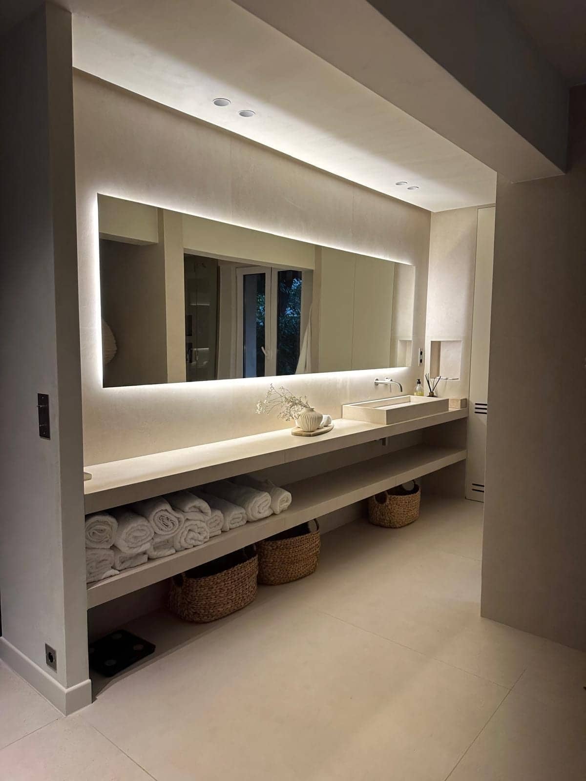 Salle de bains en béton ciré avec miroir rétroéclairé et étagère garnie de serviettes à Vincennes
