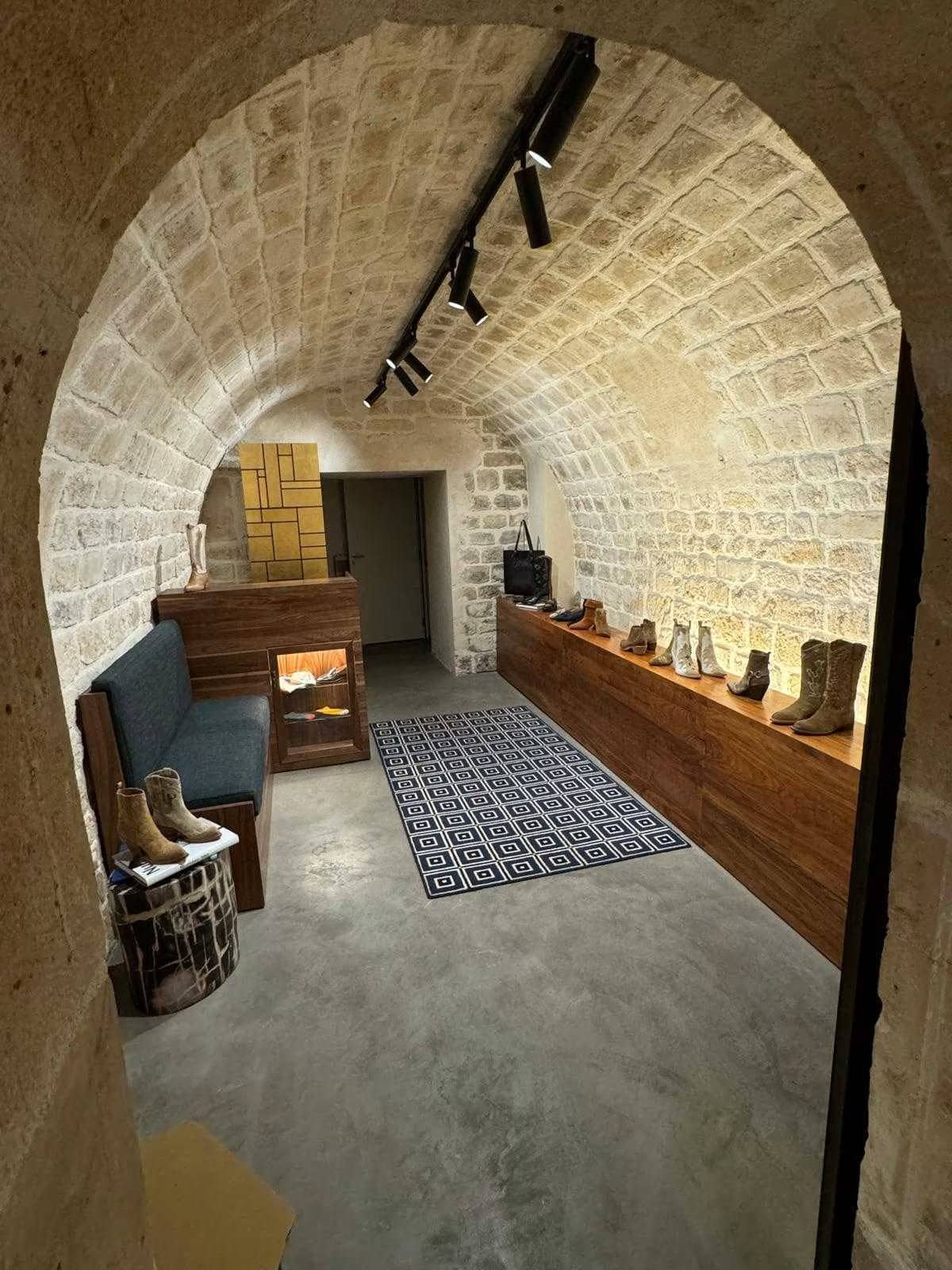 Boutique voûtée en pierre apparente avec spots sur rail, banquette, chaussures et sol en béton ciré à Paris