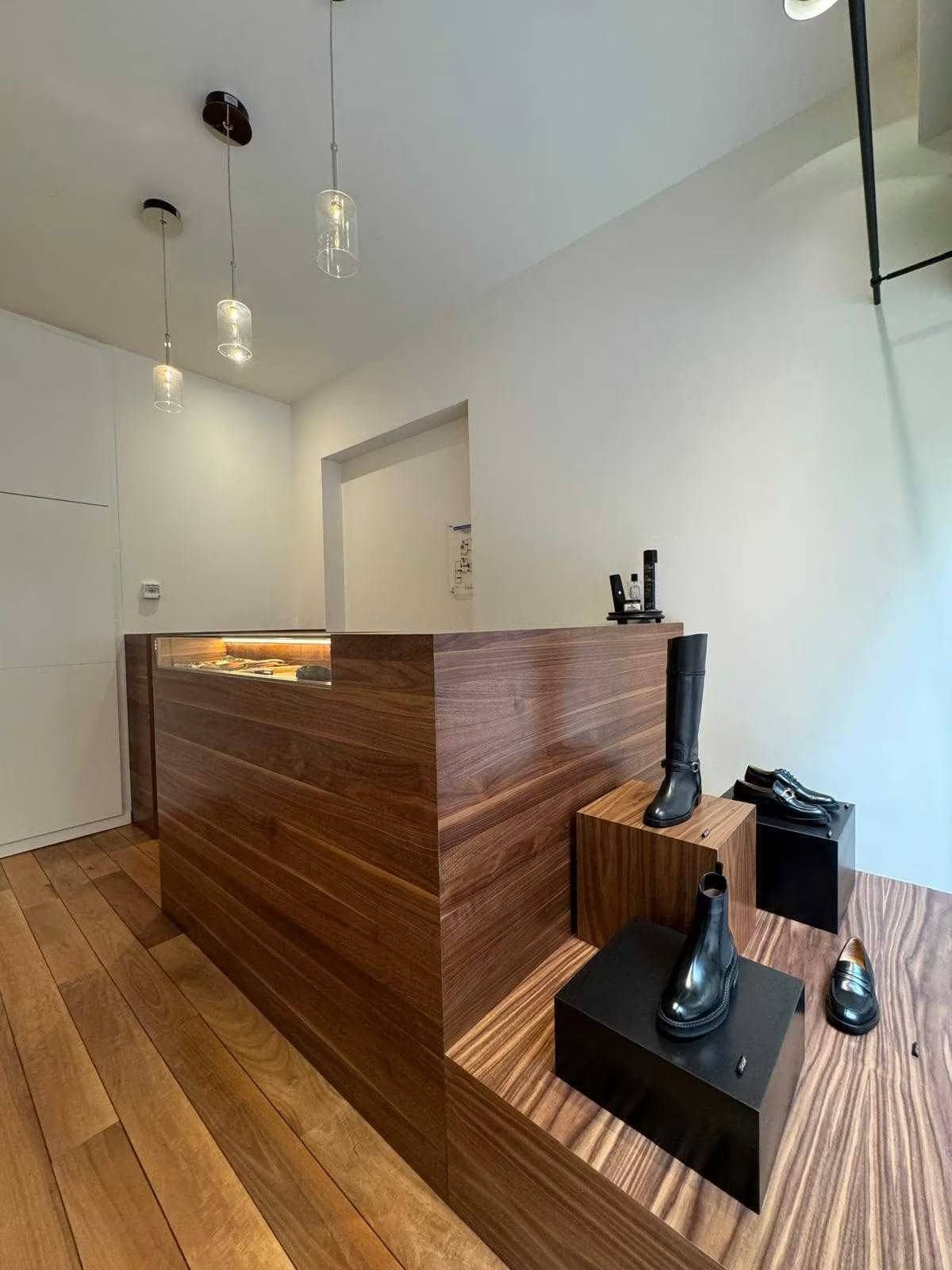 Boutique parisienne avec comptoir en bois exotique, gradins d'exposition de bottes et suspensions en verre