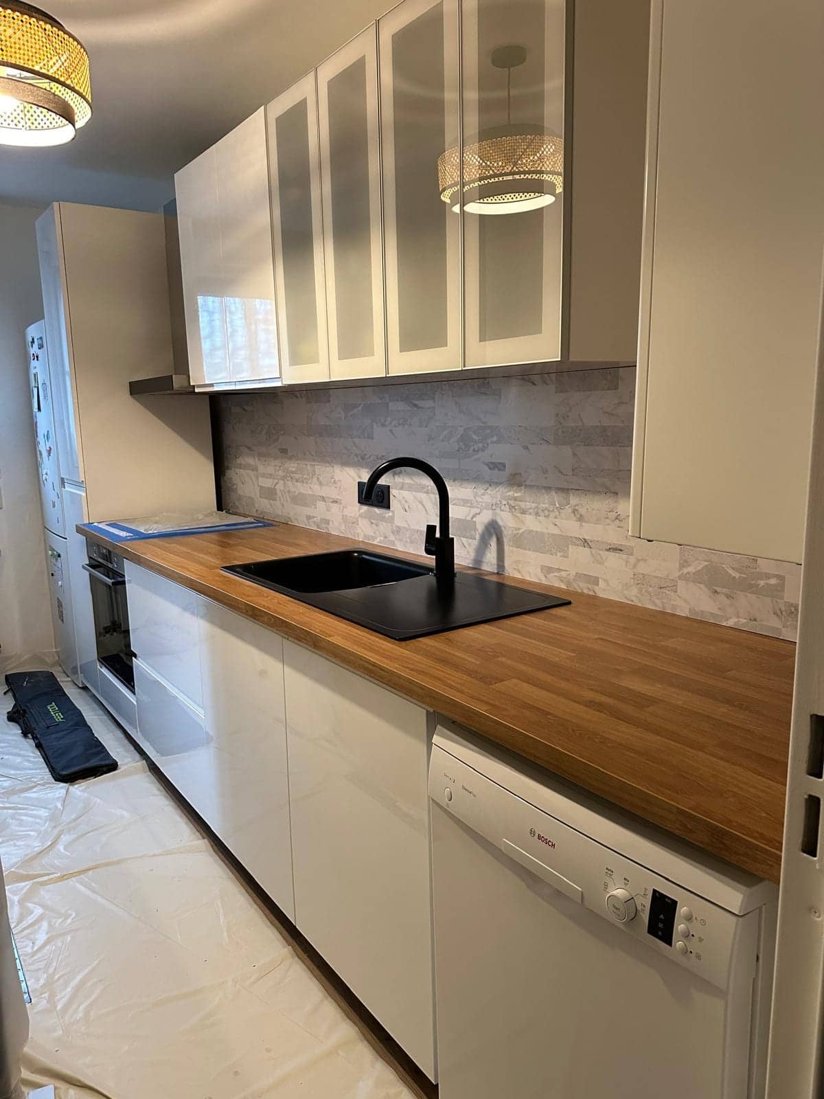 Cuisine linéaire blanche avec plan de travail en bois et robinet noir, en fin de chantier à Vincennes