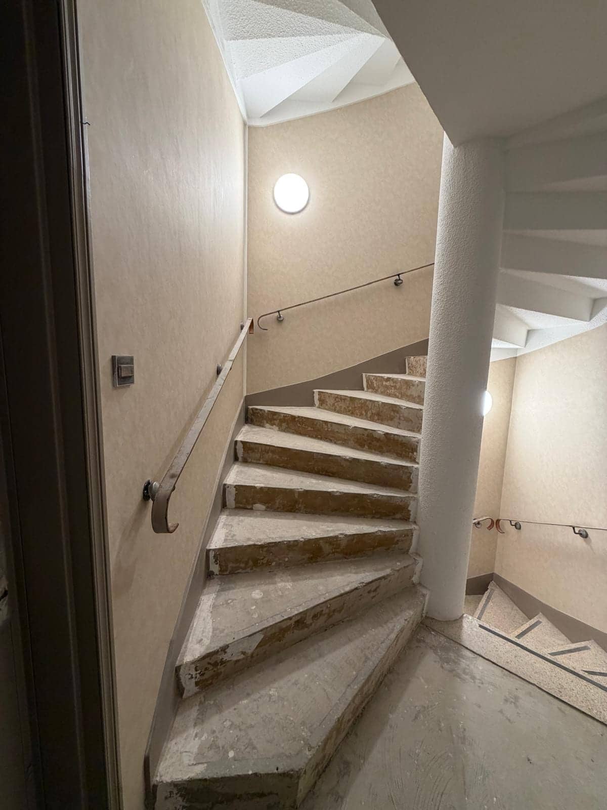 Cage d'escalier en colimaçon avec marches en pierre, main courante et mur clair rénovés