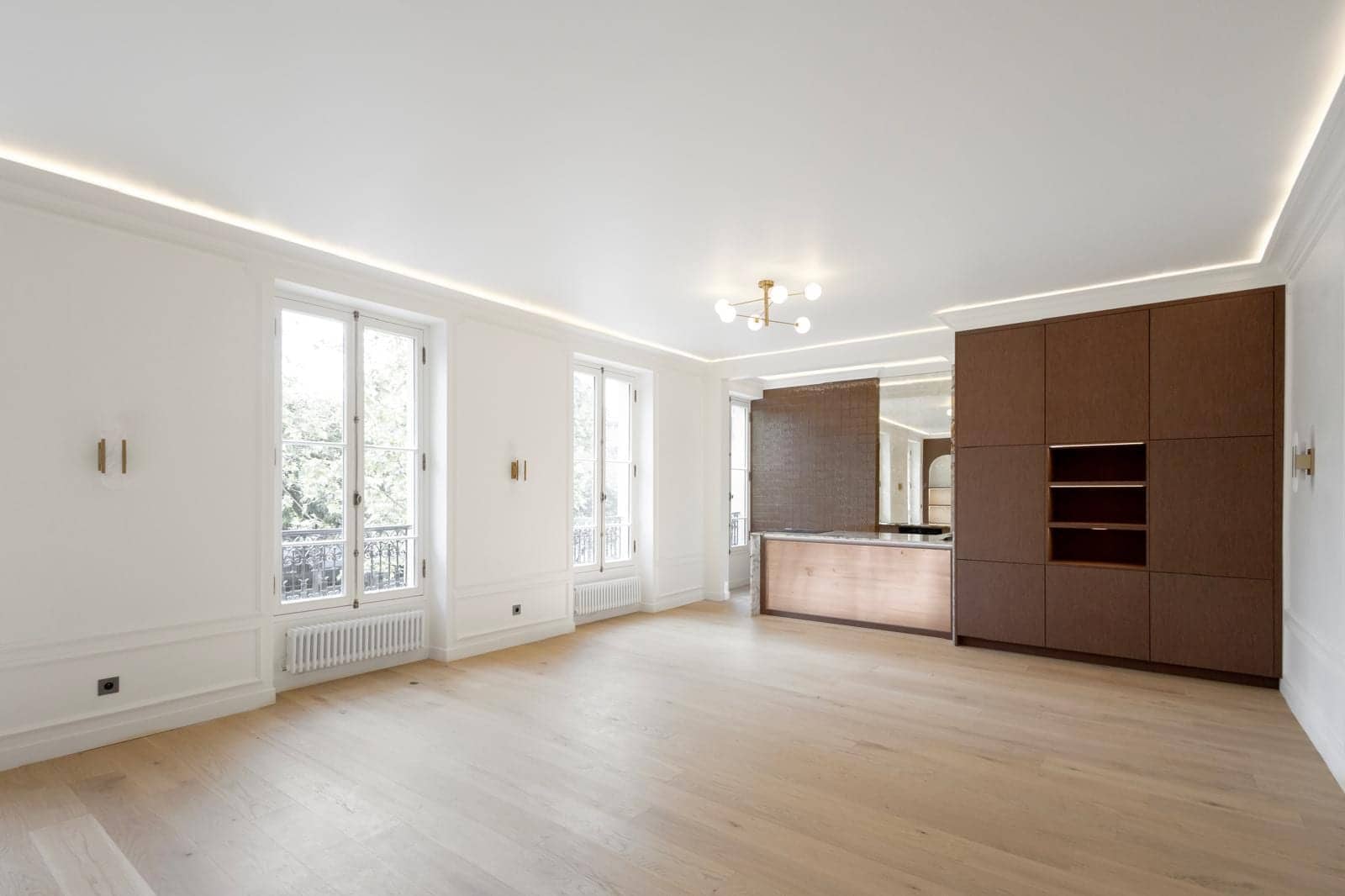 Séjour d'appartement à Versailles avec parquet, boiseries blanches, mur brun et cuisine ouverte en bois