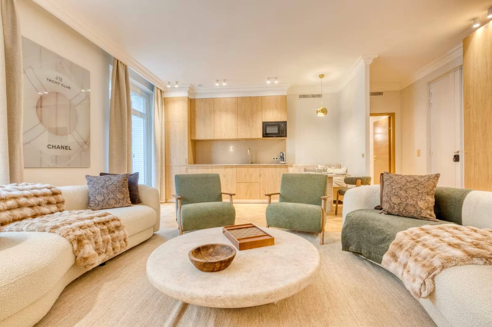 Séjour d'hôtel parisien avec canapés crème, fauteuils verts, table basse ronde et cuisine en bois