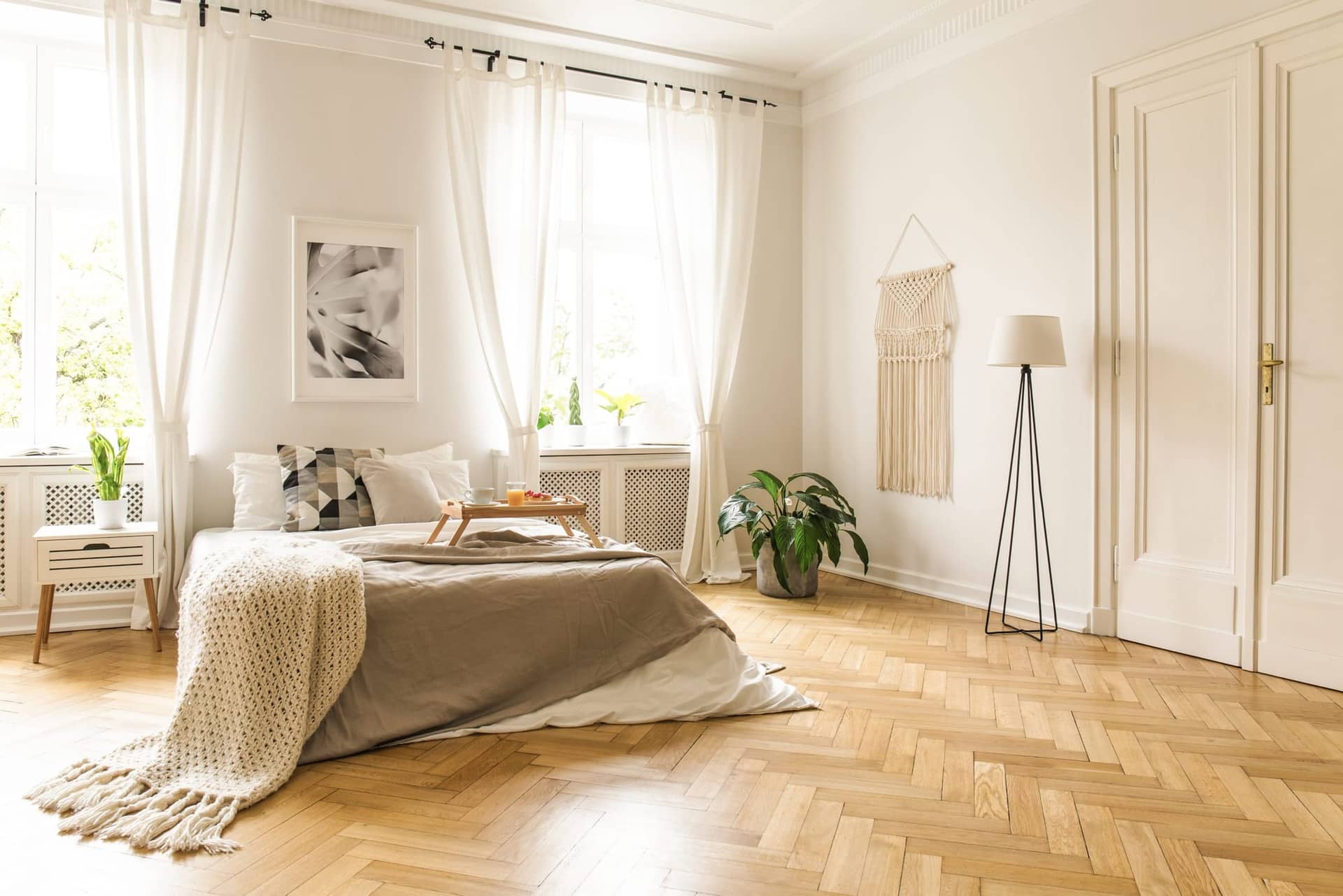 Chambre claire avec lit, rideaux blancs, parquet à bâtons rompus et porte à moulures