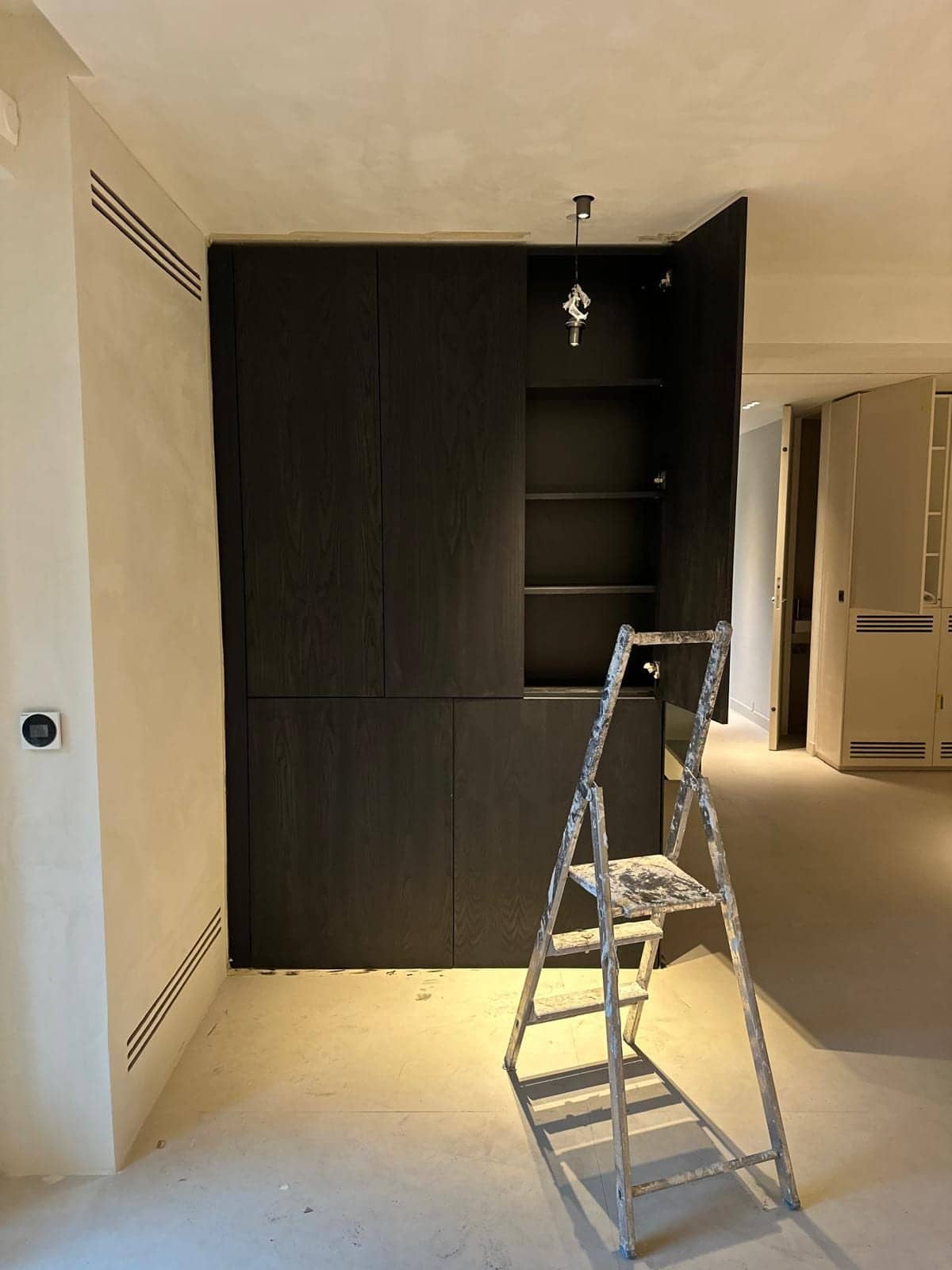 Meuble de rangement en bois sombre avec niches ouvertes et escabeau dans un appartement en travaux à Vincennes