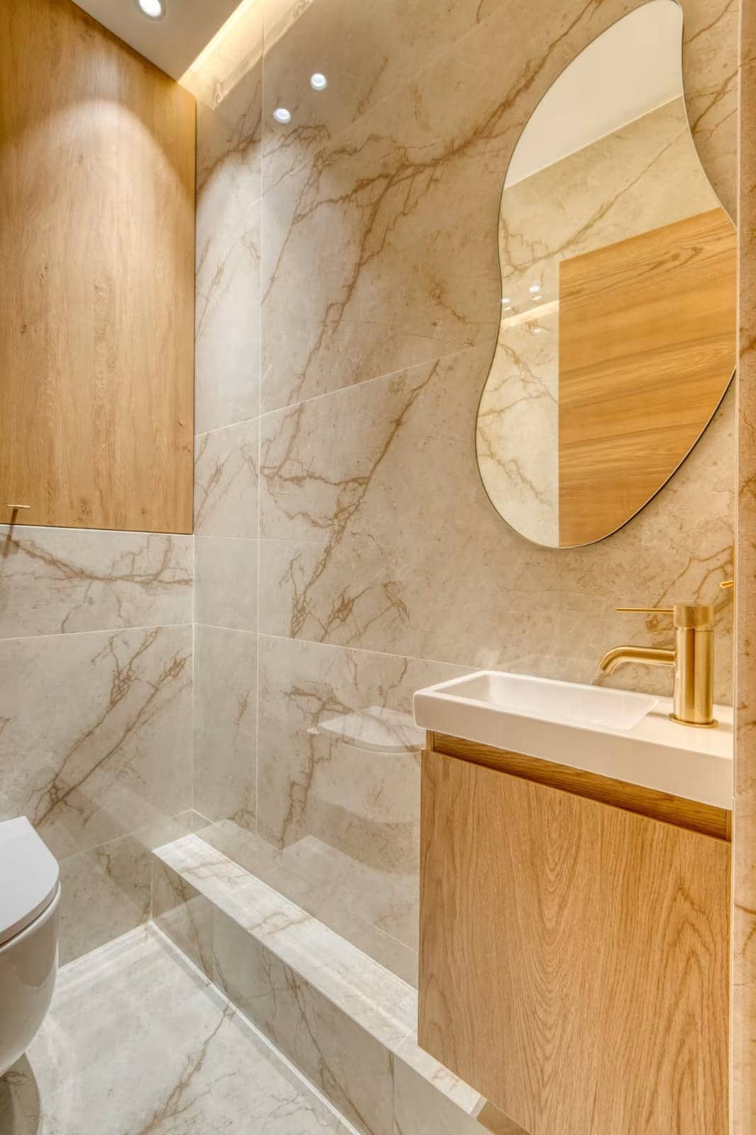 Salle d'eau en dalles effet marbre beige avec meuble en chêne et robinetterie dorée