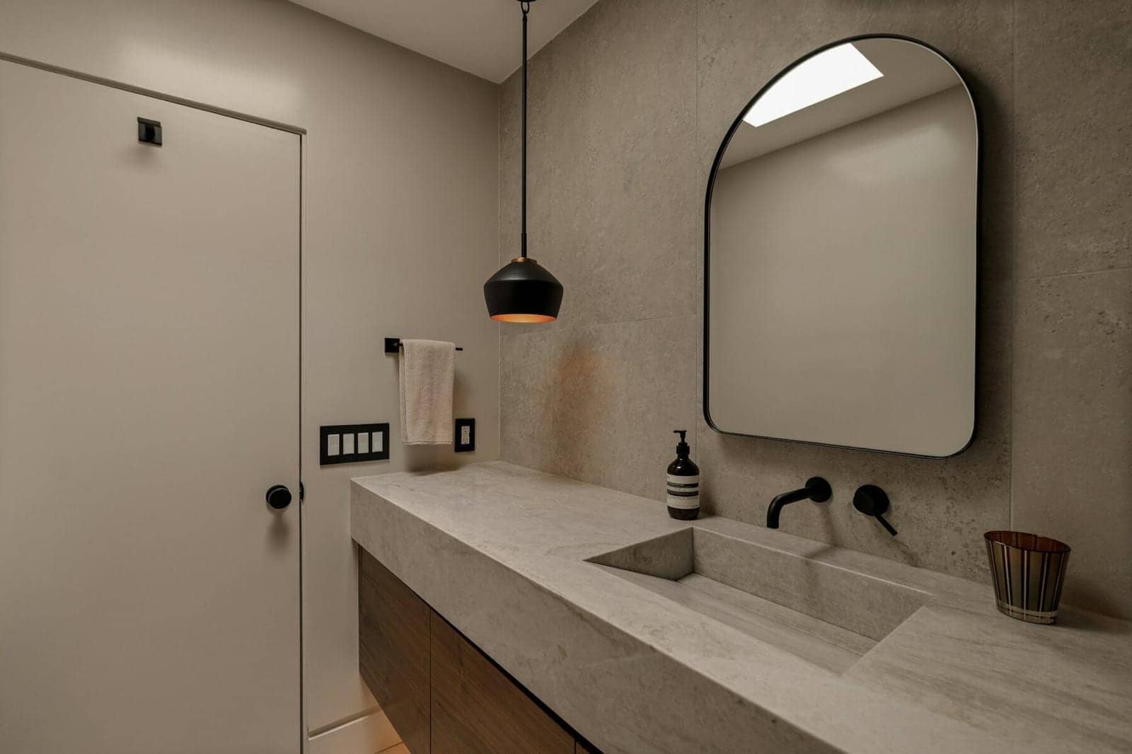 Salle de bain grise avec vasque en pierre, miroir arqué, robinetterie noire et meuble en noyer