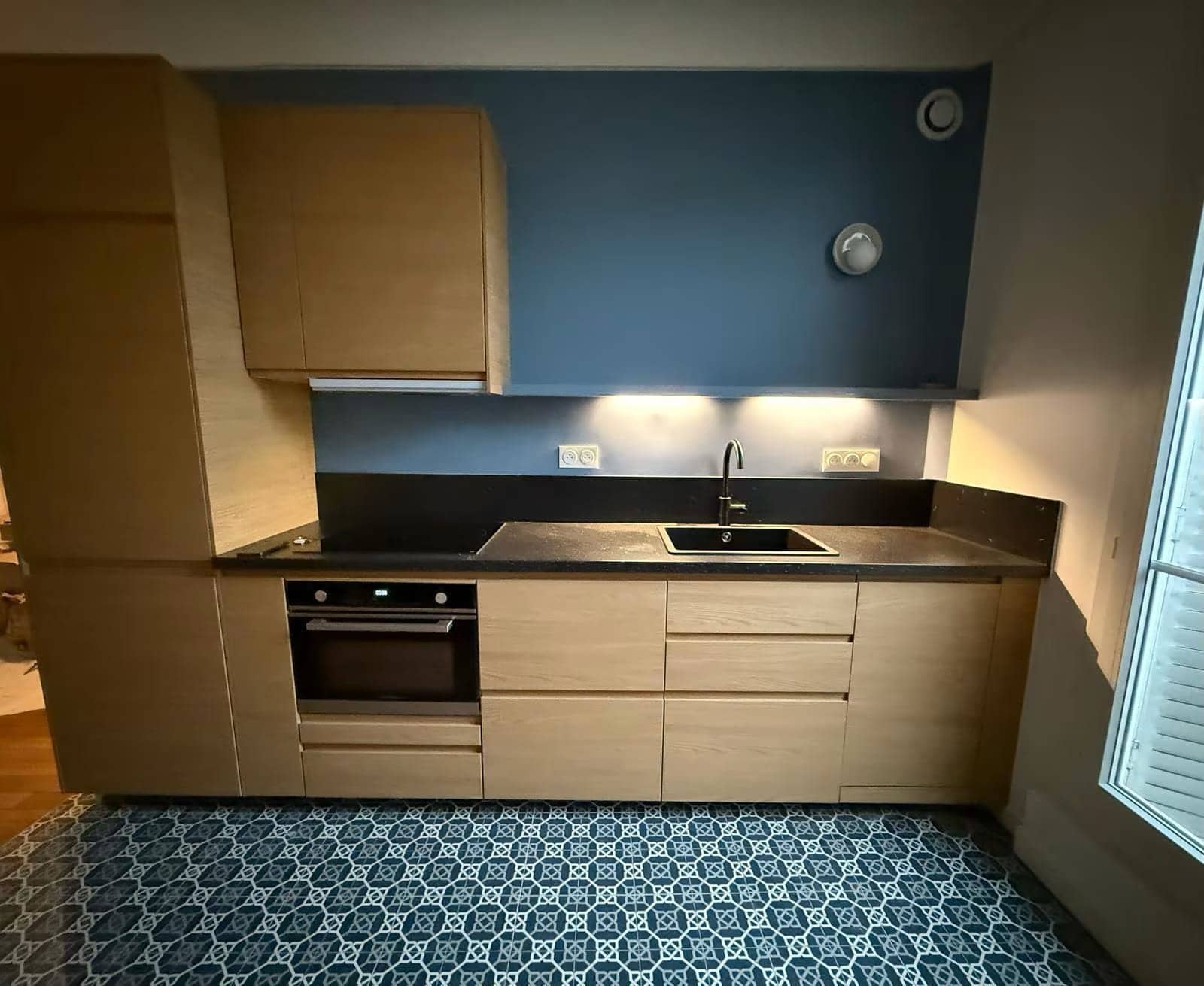 Cuisine en chêne clair avec plan de travail noir, mur bleu et carreaux de ciment bleus