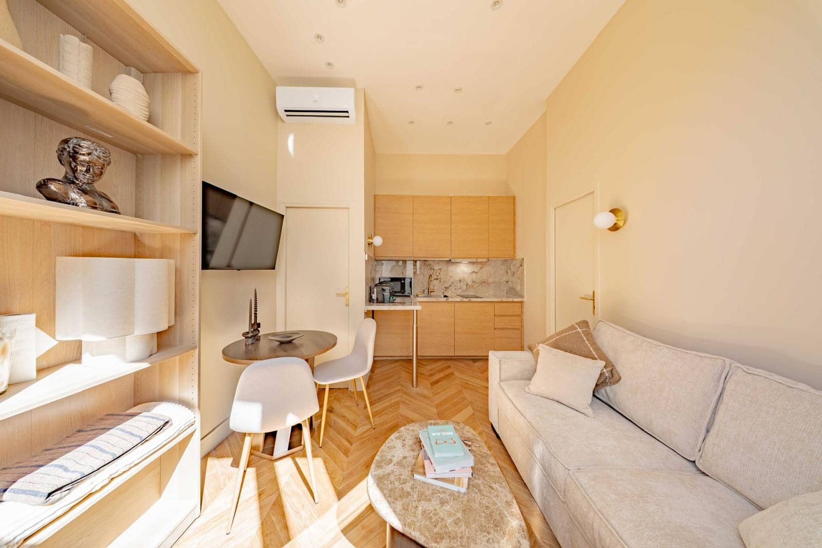 Studio locatif avec canapé, coin repas, kitchenette en bois clair et parquet en point de Hongrie