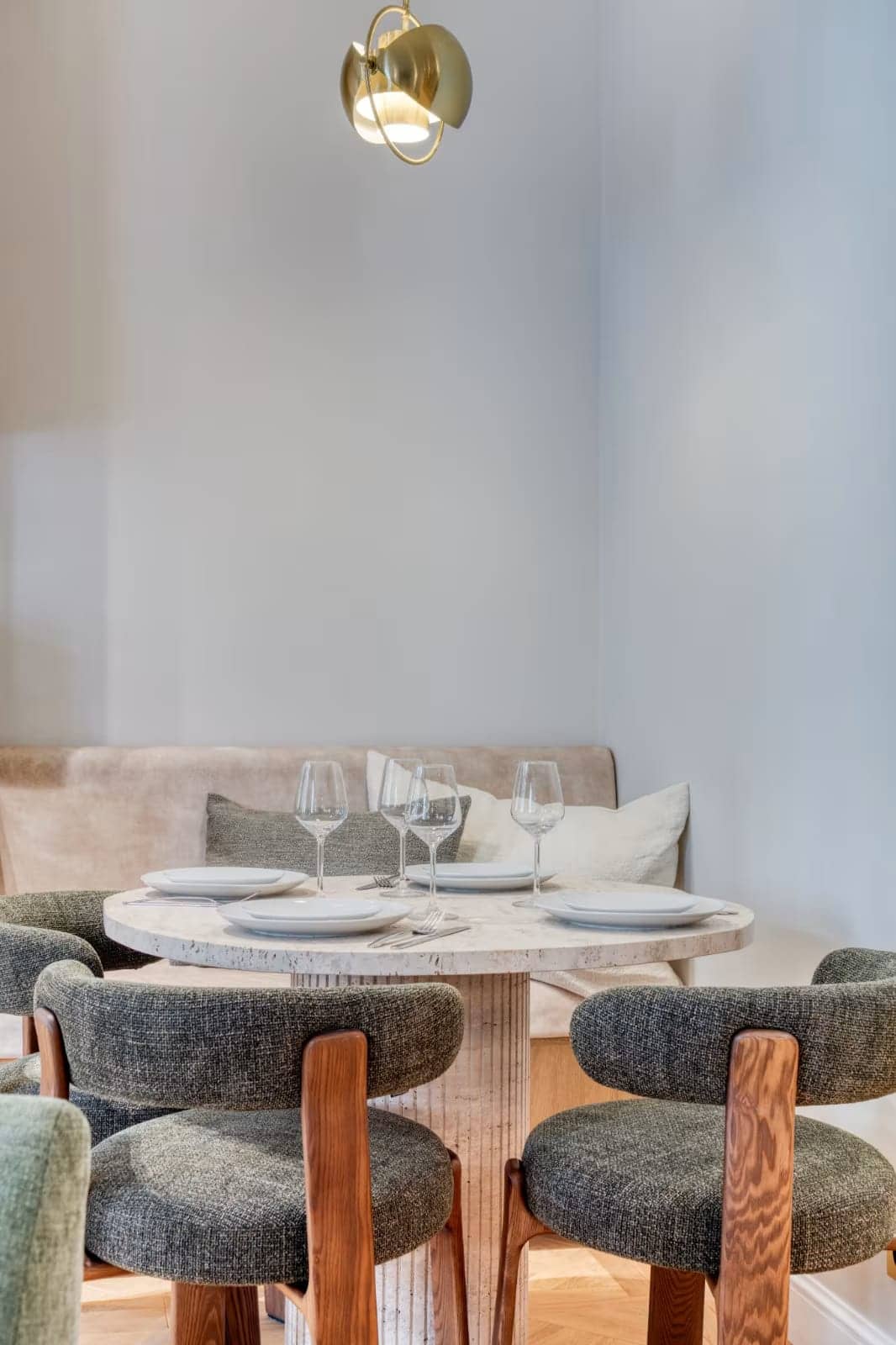 Salle à manger avec table ronde en travertin, chaises en tissu et bois et banquette