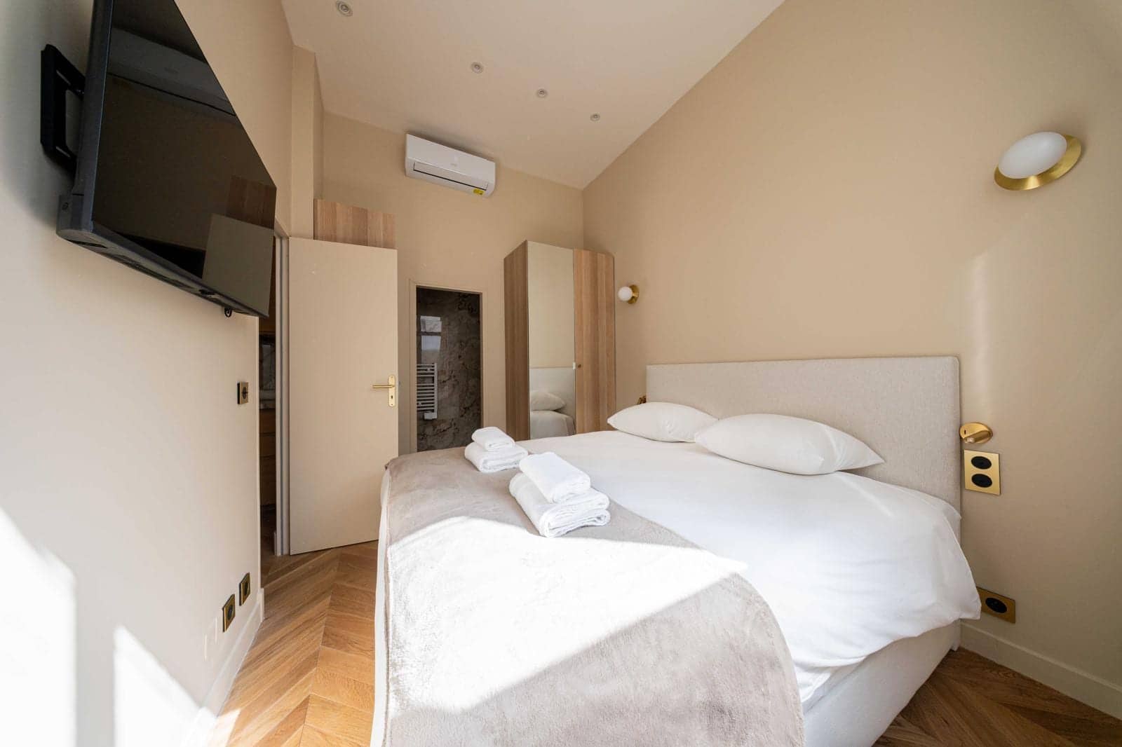 Chambre de location courte durée avec lit double, linge blanc, télévision et climatisation murale