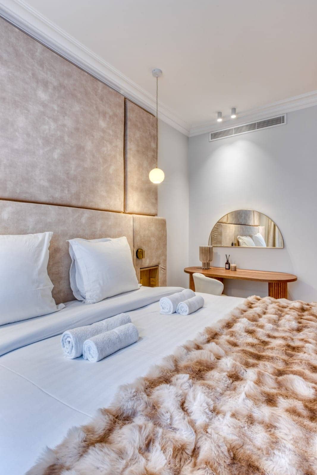Chambre avec tête de lit capitonnée beige, plaid en fausse fourrure et coiffeuse avec miroir demi-lune