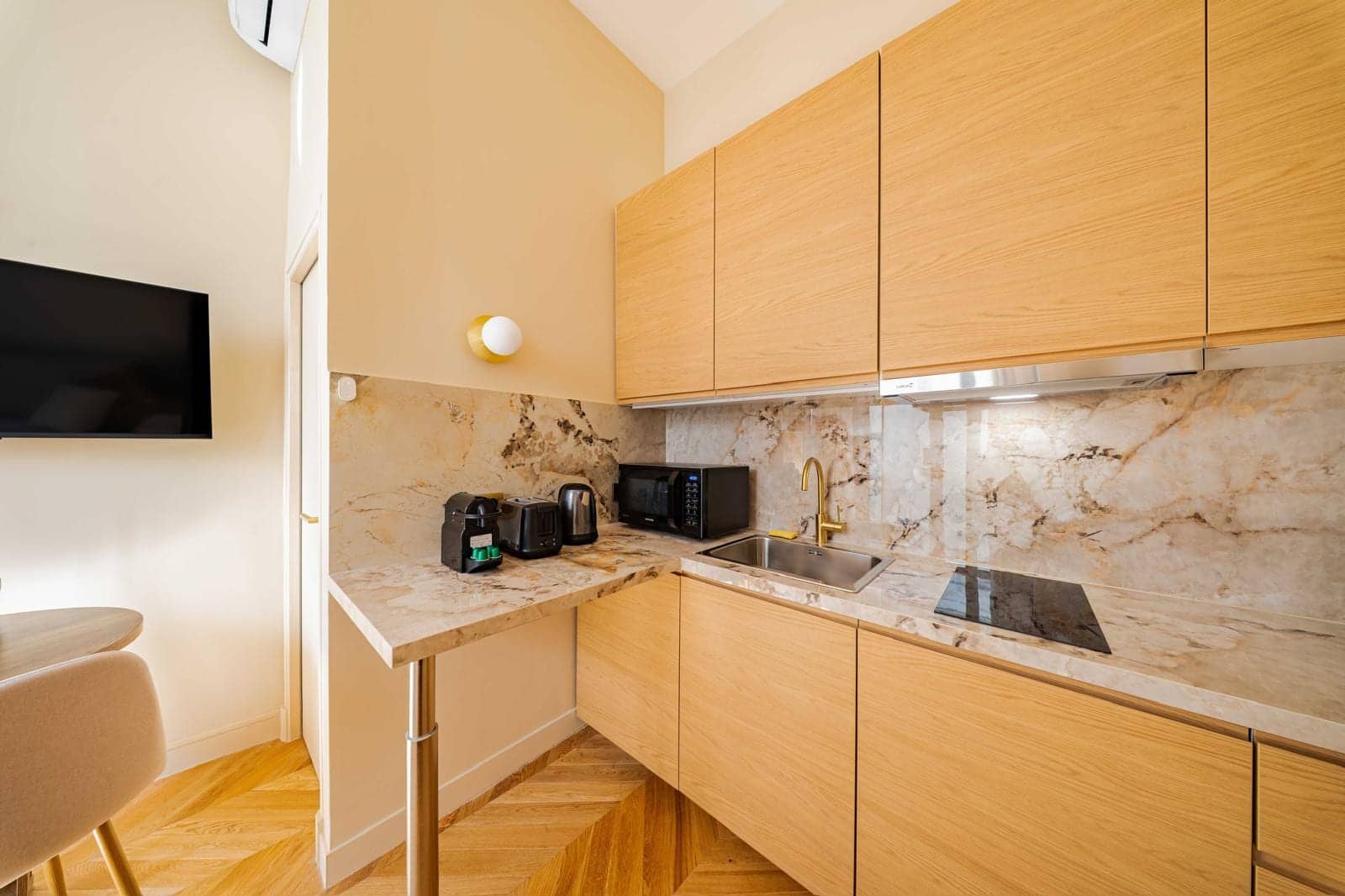 Kitchenette en bois clair avec plan de travail en marbre dans un studio locatif
