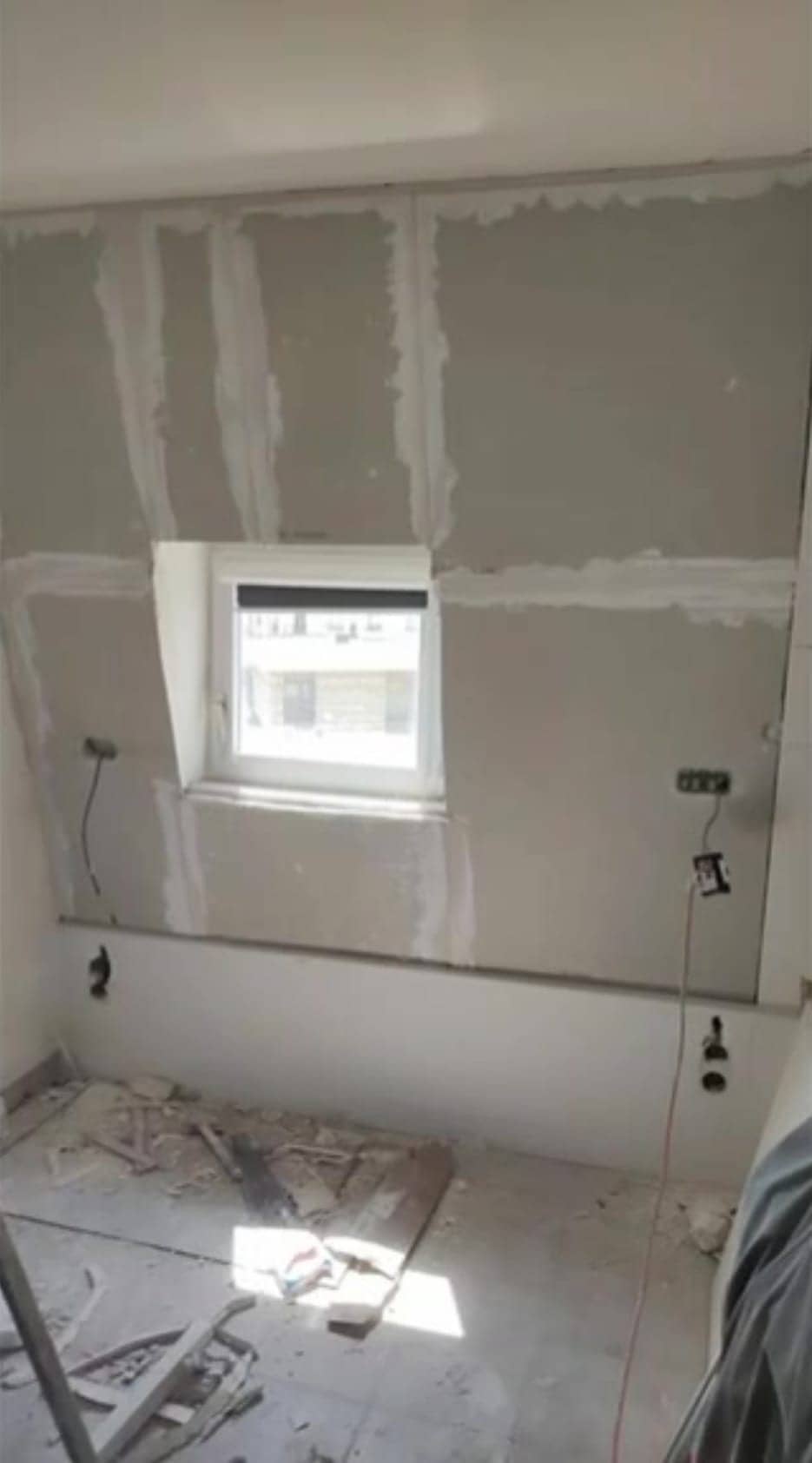 Rénovation intérieure d’un mur de façade en cours avec isolant et joints en placoplâtre autour d’une petite fenêtre, outils et câbles au sol. Ravalement paris obligation intégré.