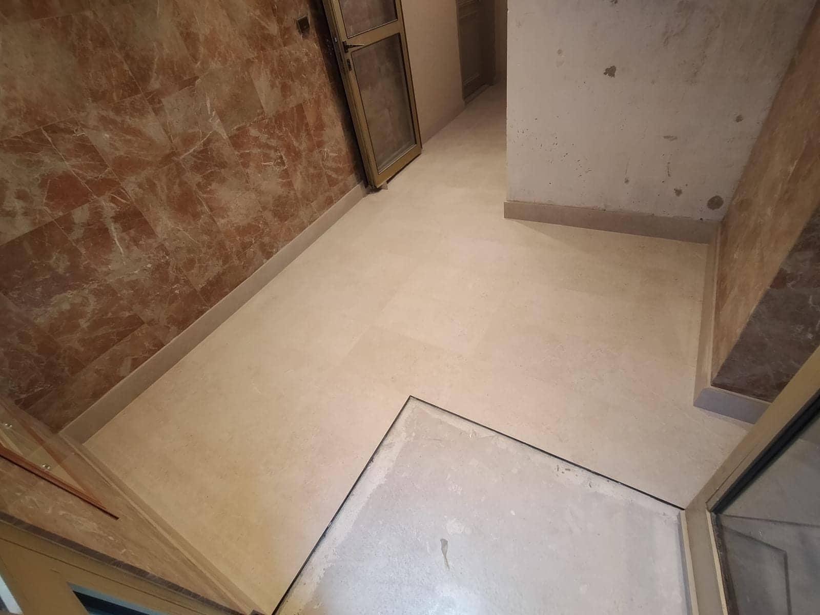 Hall d'immeuble en travaux avec grand carrelage clair posé et mur en marbre rose