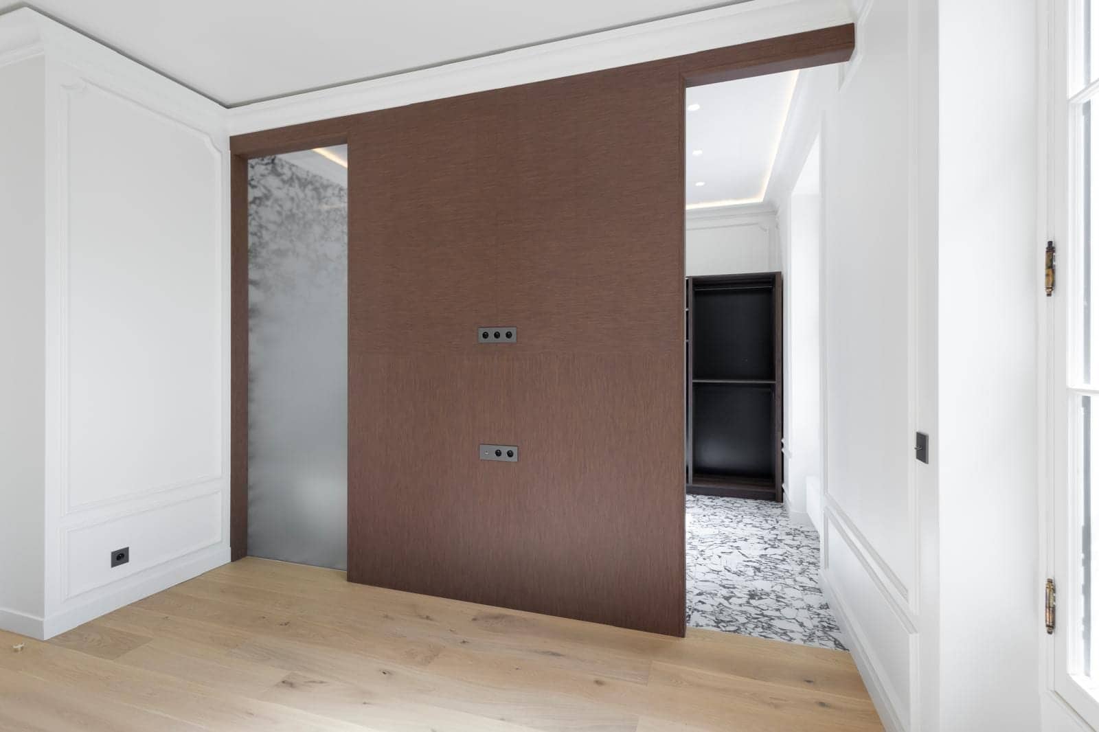 Cloison coulissante en bois brun entre chambre et dressing au sol en marbre noir et blanc