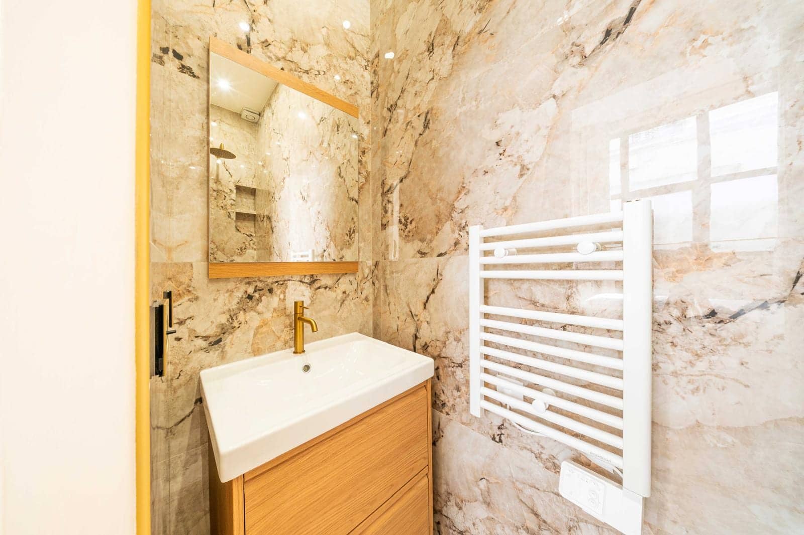 Salle d'eau de studio avec vasque blanche sur meuble en bois et murs en marbre veiné