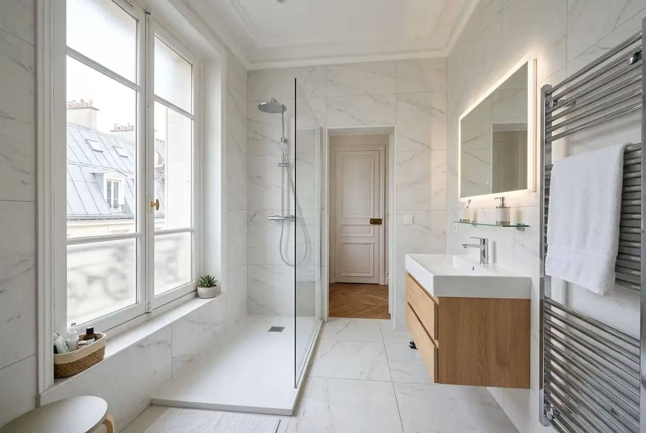 Salle de bains lumineuse et contemporaine, avec douche à l’italienne, meuble lavabo bois et miroir éclairé, radiateur sèche-serviettes et grand fenêtre Paris 15. Rénovation salle de bain paris 15 prête à l’installation.