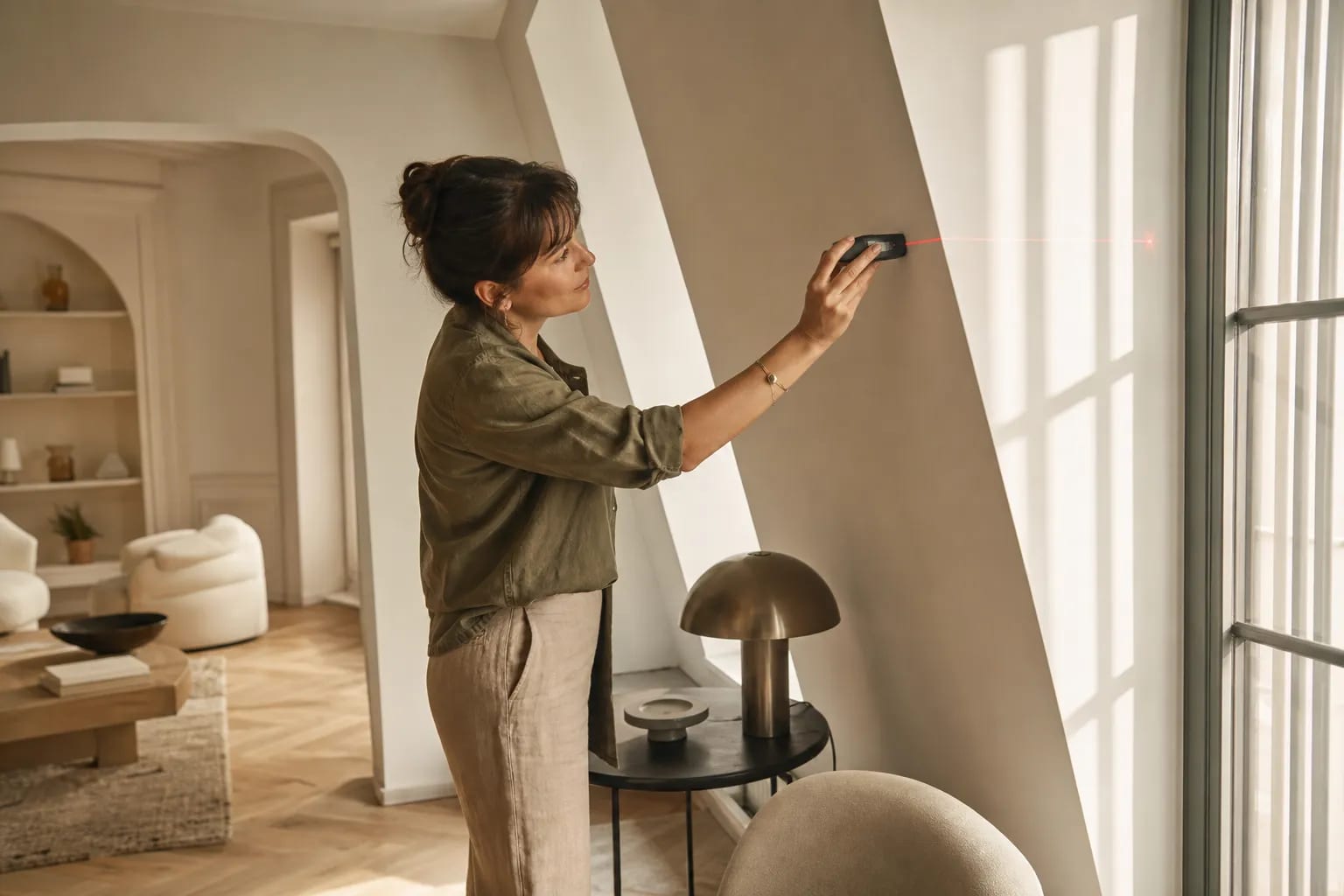 Consultante en agencement intérieur appartement paris utilisant un laser pour mesurer une façade intérieure lumineuse et moderne.
